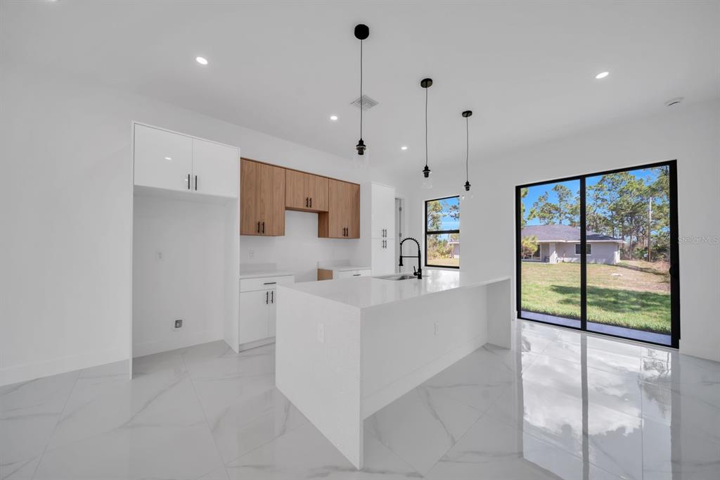 A modern kitchen features white cabinets, wood-toned upper cabinets, a quartz island, and sliding glass doors — 635 SUMMIT AVENUE S, LEHIGH ACRES, FL