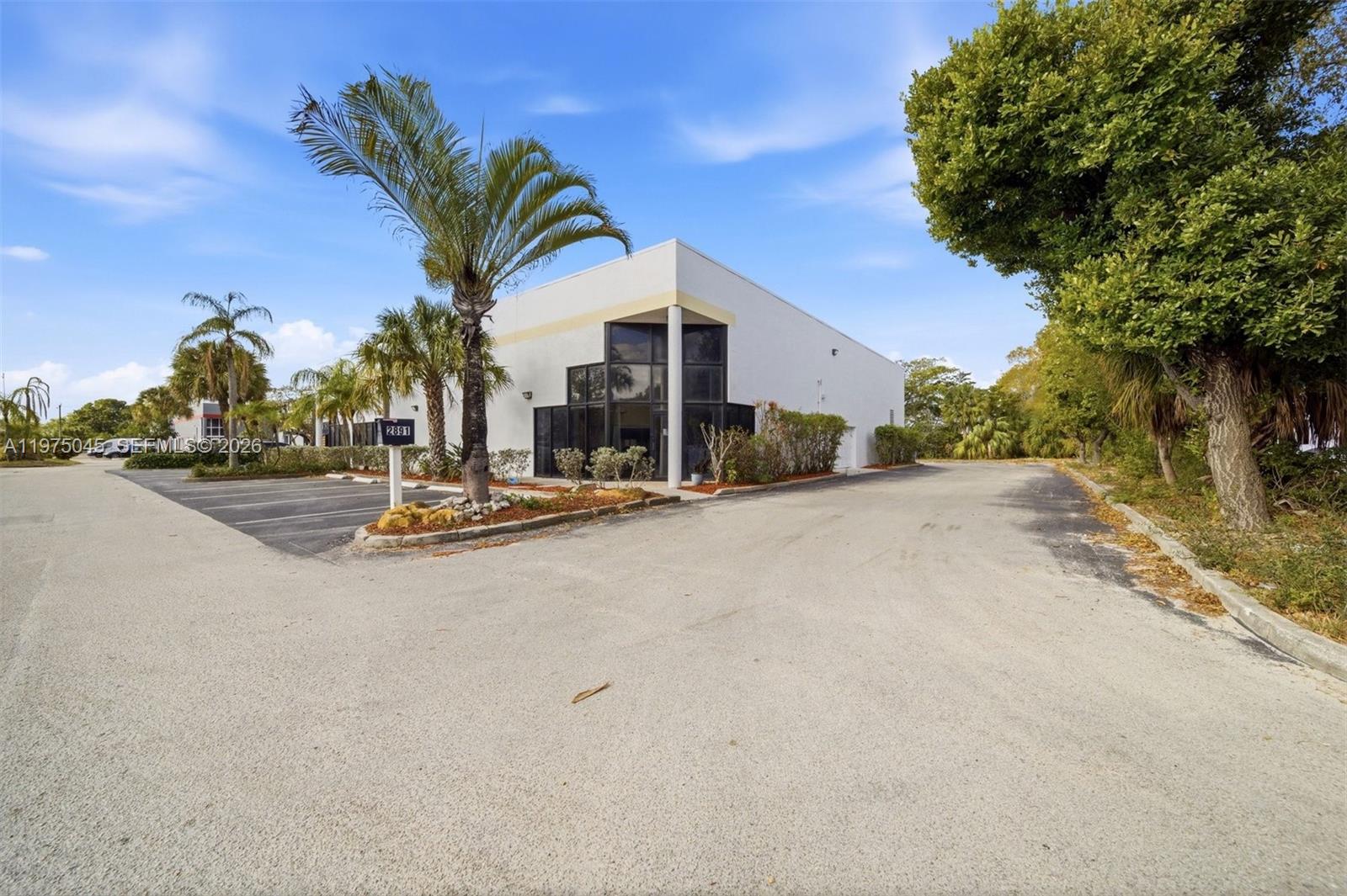 A white commercial building with a glass corner entrance stands next to a paved parking lot — 2891 NW 22nd Ter, Pompano Beach FL 33069, POMPANO BEACH, FL