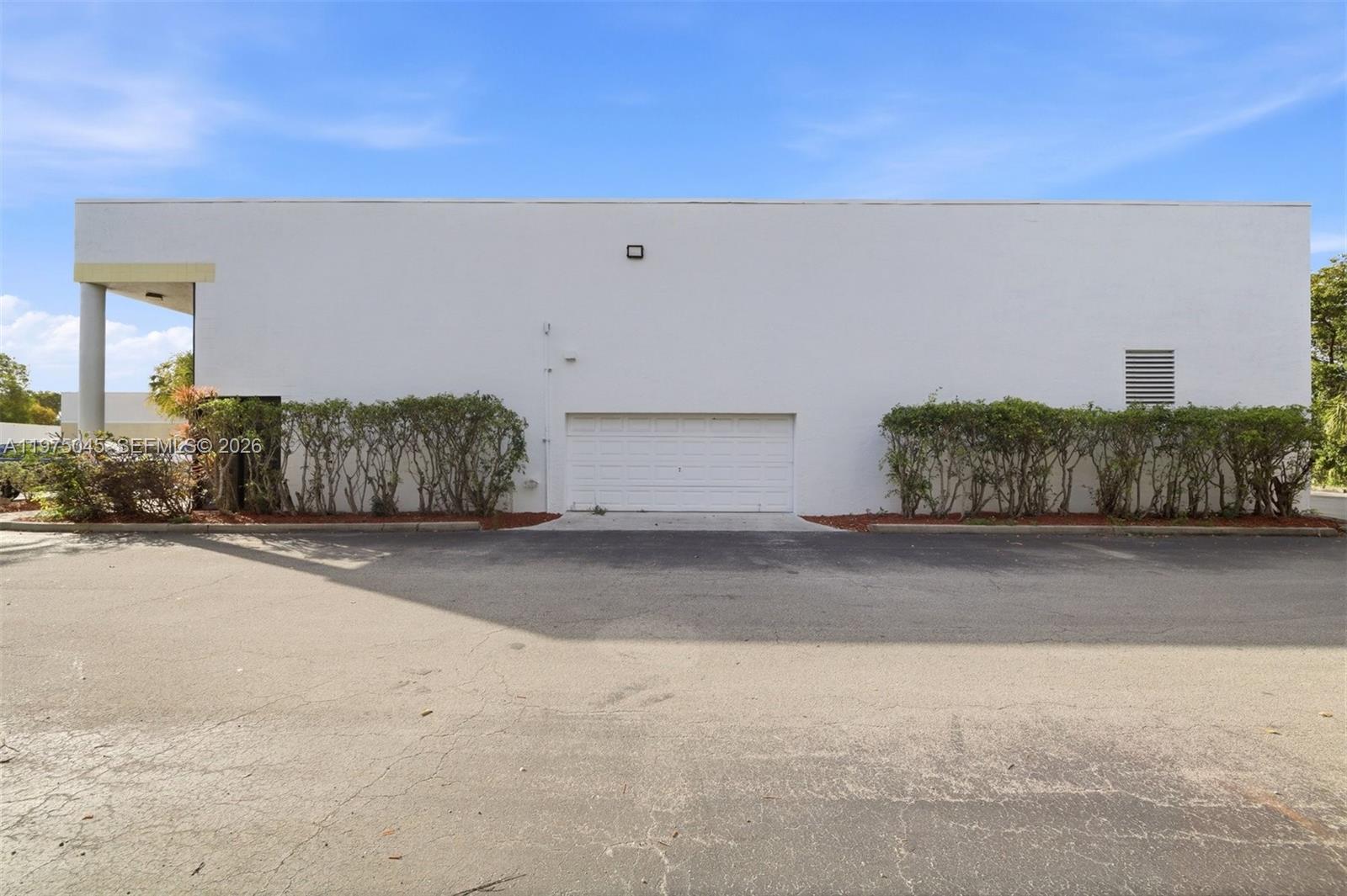 A white commercial building exterior features a central garage door and surrounding landscaping — 2891 NW 22nd Ter, Pompano Beach FL 33069, POMPANO BEACH, FL