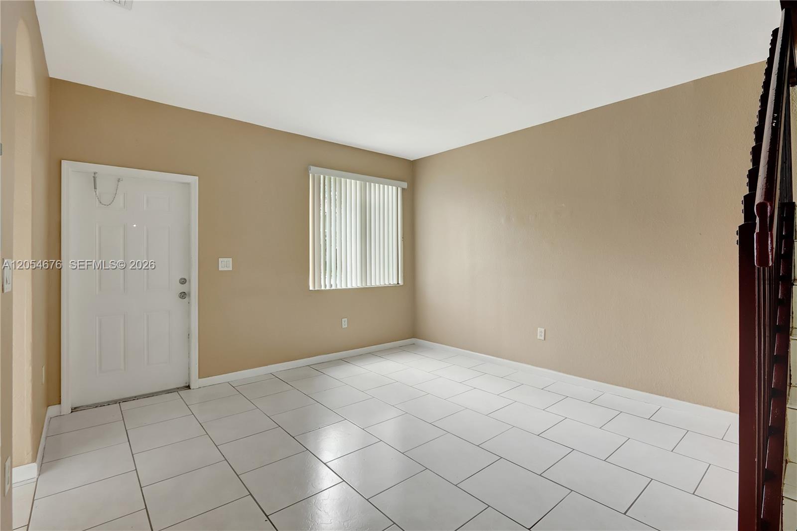 An empty room features beige walls, white tile flooring, a window with blinds, and a door — 2874 SE 15th Rd # 52, Homestead FL 33035, HOMESTEAD, FL