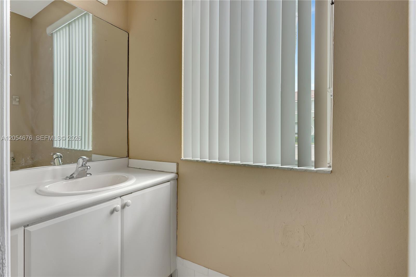 A bathroom features a white vanity with a sink, a mirror, and vertical window blinds — 2874 SE 15th Rd # 52, Homestead FL 33035, HOMESTEAD, FL