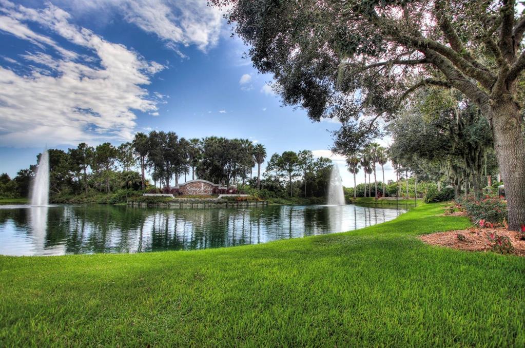 A pond with two fountains sits in front of a landscaped entrance sign and trees — 5301 MAHOGANY RUN AVENUE UNIT 1023, SARASOTA, FL