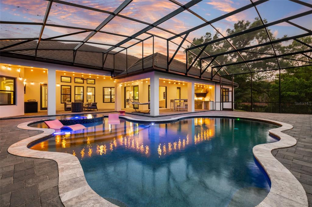 A screened-in patio features a swimming pool with a spa and an outdoor kitchen area — 1 STONE GATE S, LONGWOOD, FL