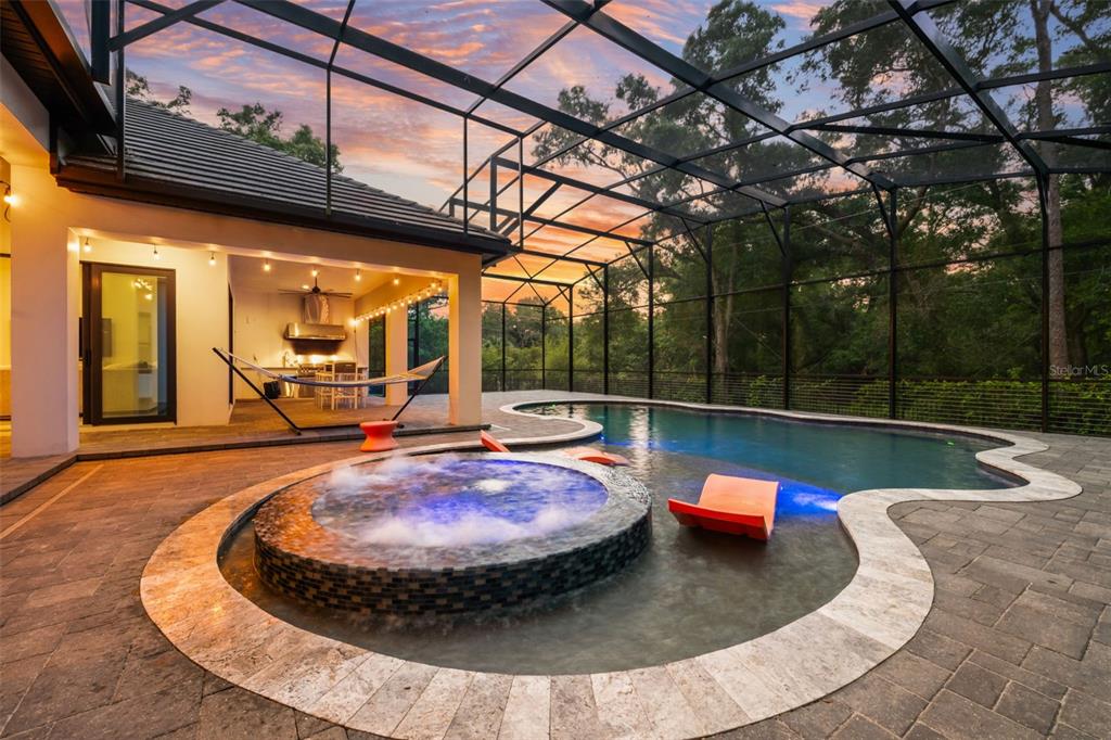 A screened-in patio features a swimming pool with an integrated hot tub and lounge chairs — 1 STONE GATE S, LONGWOOD, FL