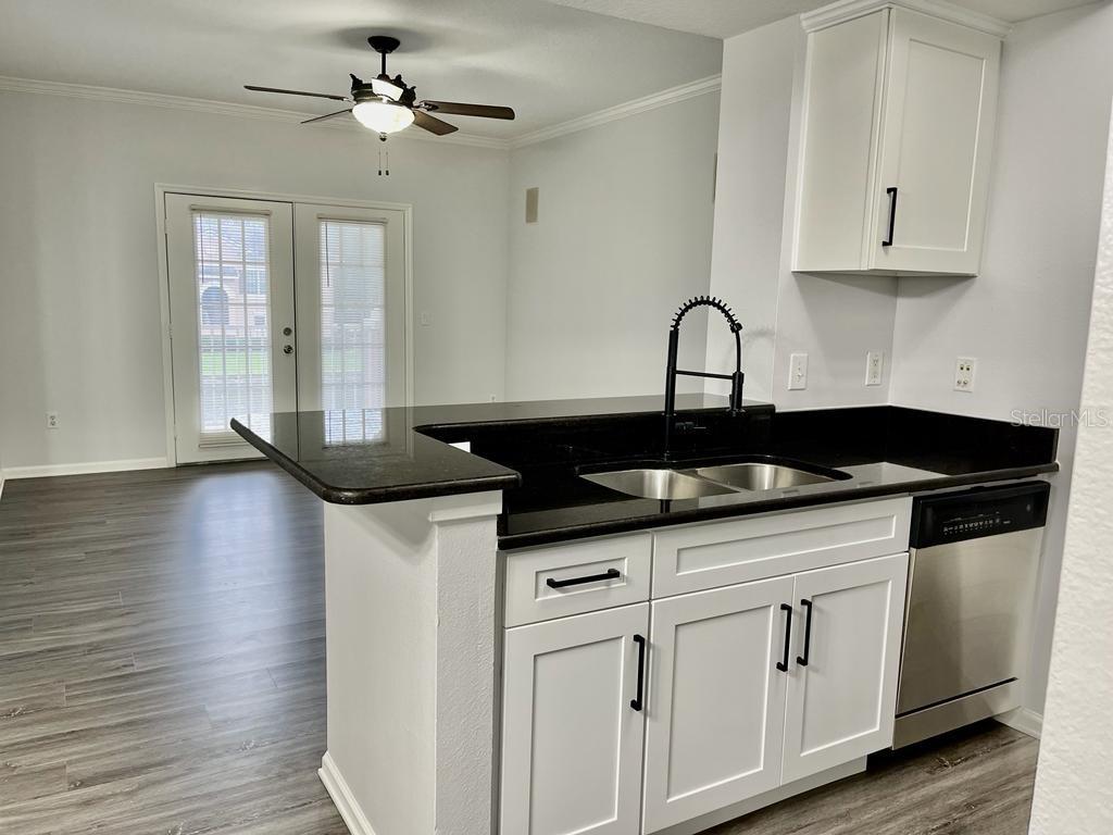 A kitchen with white cabinets, black countertops, and a sink overlooking an adjacent living area — 14316 FREDRICKSBURG DRIVE UNIT 514, ORLANDO, FL