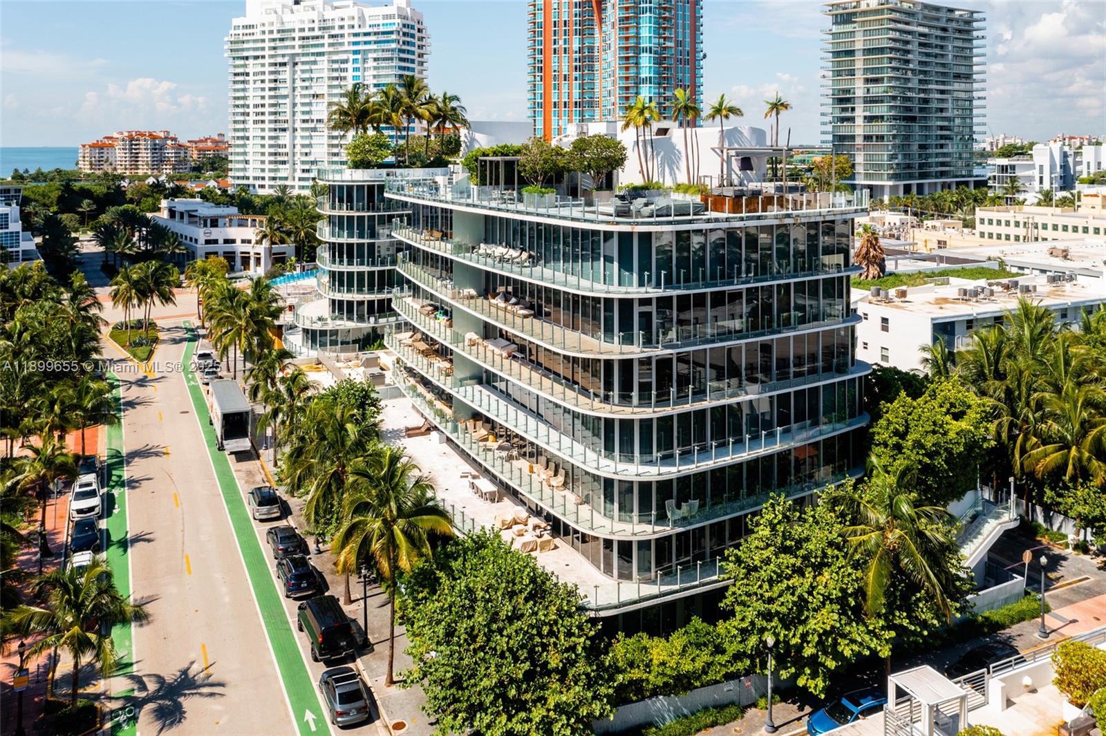 An aerial view shows a modern multi-story building with glass balconies and a rooftop terrace — 1 Collins Ave # 207, Miami Beach FL 33139, MIAMI BEACH, FL