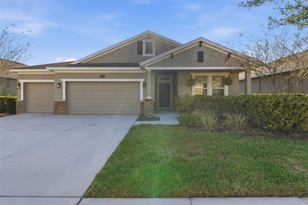 A single-story house with a tan exterior, stone accents, a three-car garage, and landscaping — 404 W VICTORIA TRAILS BLVD, DELAND, FL