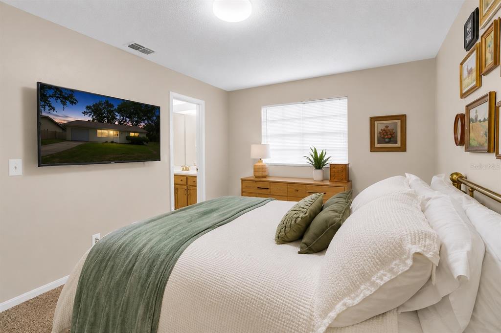 A bedroom features a bed, a wall-mounted television, a dresser, and a doorway to a bathroom — 1733 LARKIN ROAD, SPRING HILL, FL