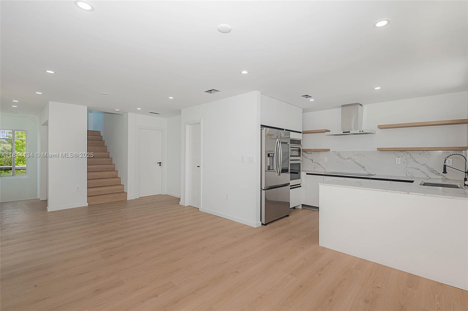 A modern kitchen features white cabinetry, marble-patterned countertops, stainless steel appliances, and open wood shelving — 1975 Calais Dr # 1, Miami Beach FL 33141, MIAMI BEACH, FL