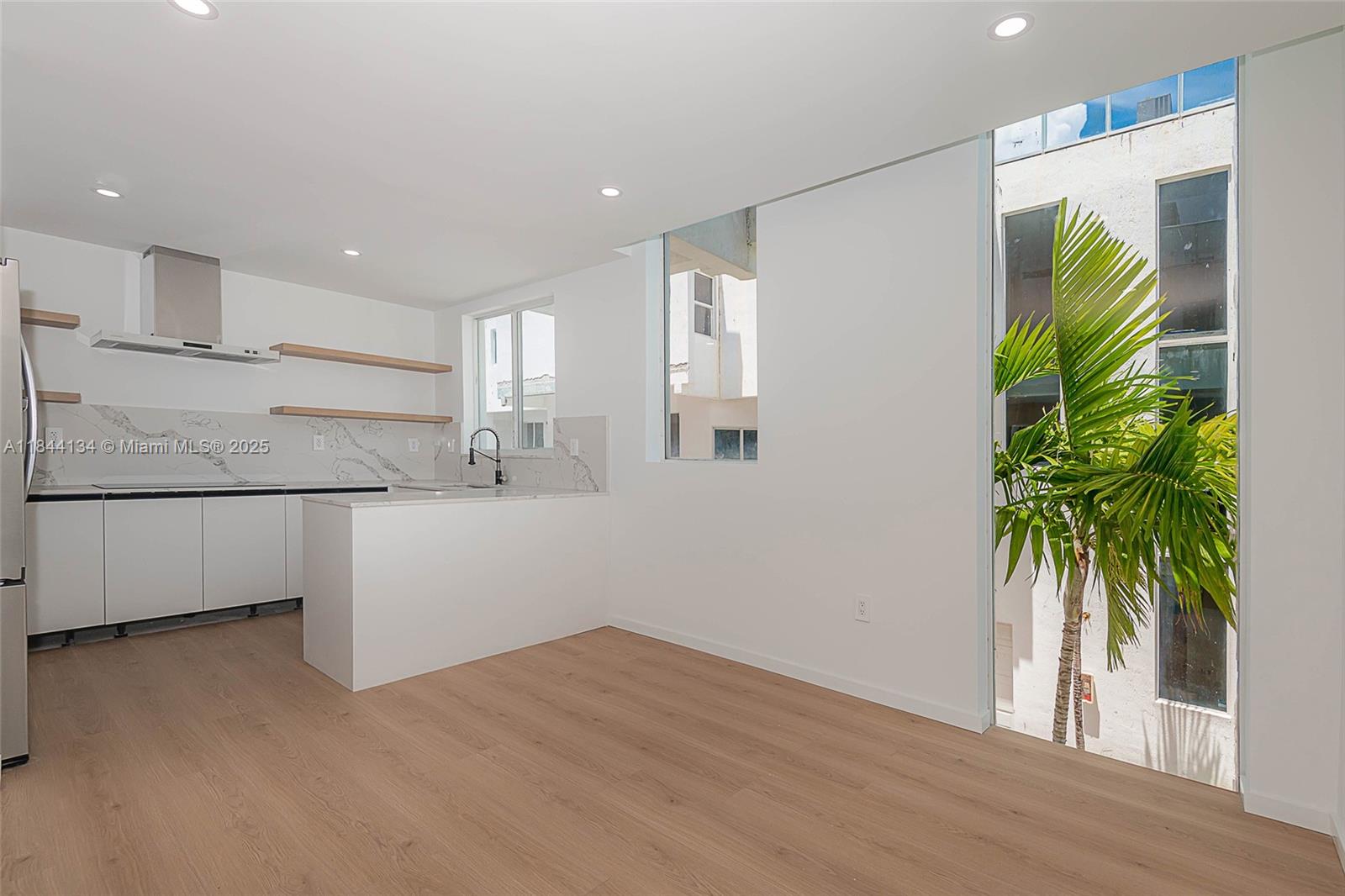 A modern kitchen with white cabinetry, marble-style backsplash, and light wood flooring opens to stairs — 1975 Calais Dr # 1, Miami Beach FL 33141, MIAMI BEACH, FL