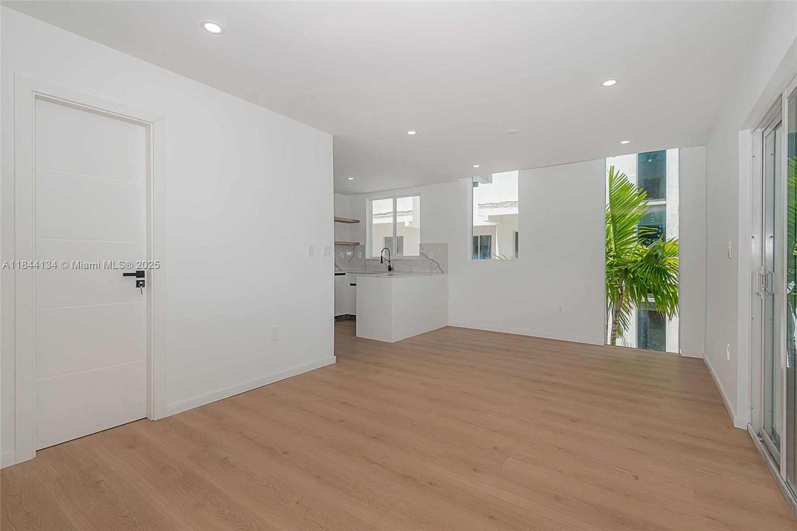 A modern kitchen features white cabinets, marble-style countertops, open wood shelving, and an adjacent atrium — 1975 Calais Dr # 1, Miami Beach FL 33141, MIAMI BEACH, FL