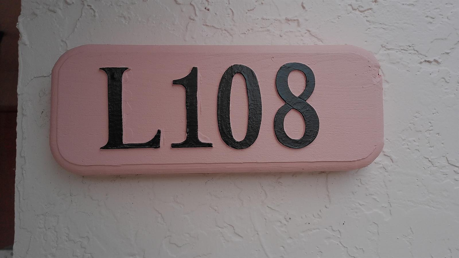 A pink rectangular sign with the black text L108 is mounted on a textured wall — 3180 Leewood Terrace # L108, Boca Raton FL 33431, BOCA RATON, FL