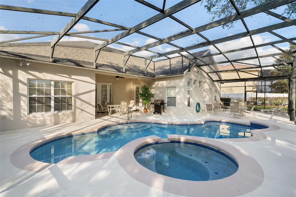 A screened-in patio features a swimming pool and attached hot tub behind a house — 7939 SEA PEARL CIRCLE, KISSIMMEE, FL