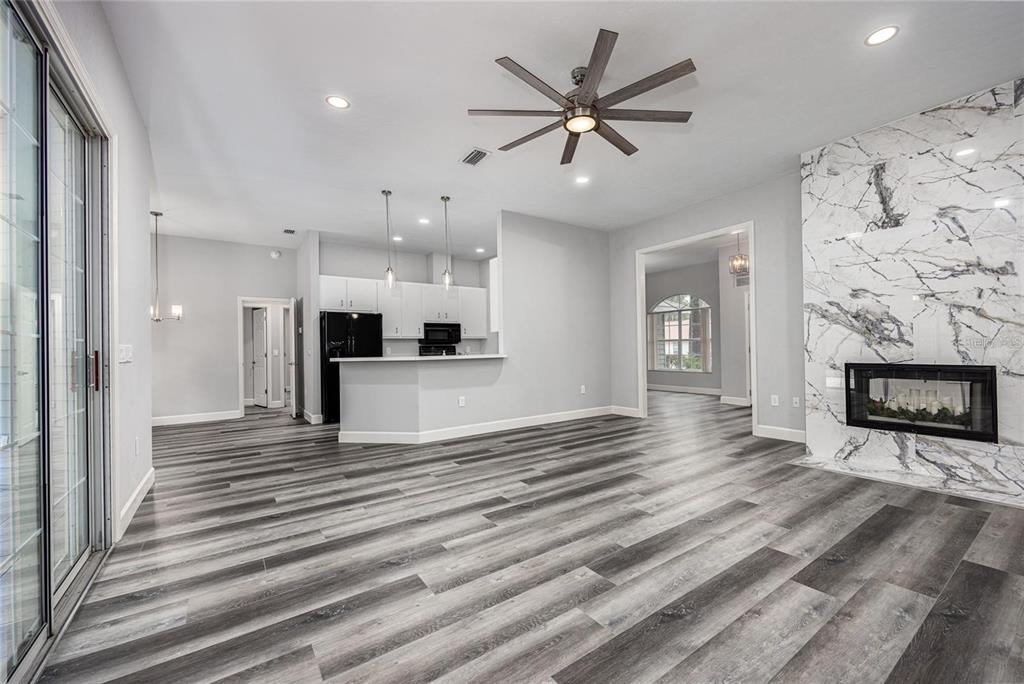 An open-concept living room features wood-look flooring, a marble fireplace, and an adjacent kitchen area — 2103 SW 75TH TERRACE, GAINESVILLE, FL