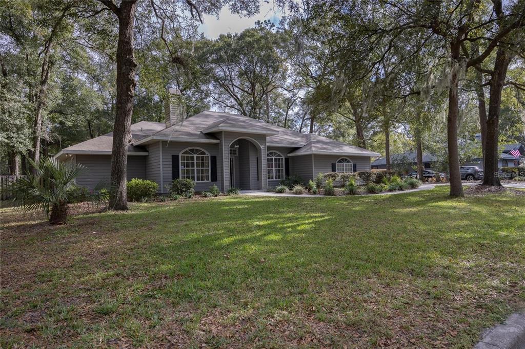 A single-story gray house with a prominent arched entryway sits on a wooded, grassy lot — 2103 SW 75TH TERRACE, GAINESVILLE, FL