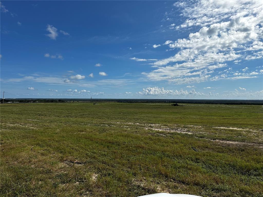 A wide, flat, grassy field under a bright blue sky with scattered clouds — SCENIC HIGHWAY N, FROSTPROOF, FL