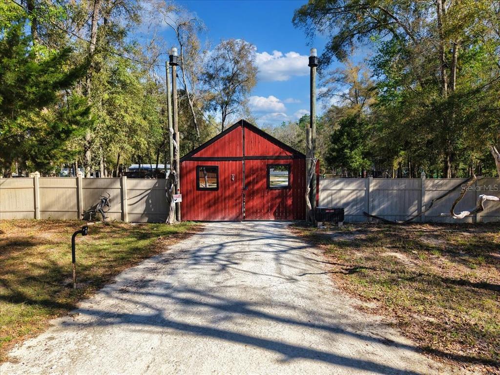 A red barn-style gate stands at the end of a gravel driveway between two fences — 5850 NW 50TH STREET, BELL, FL