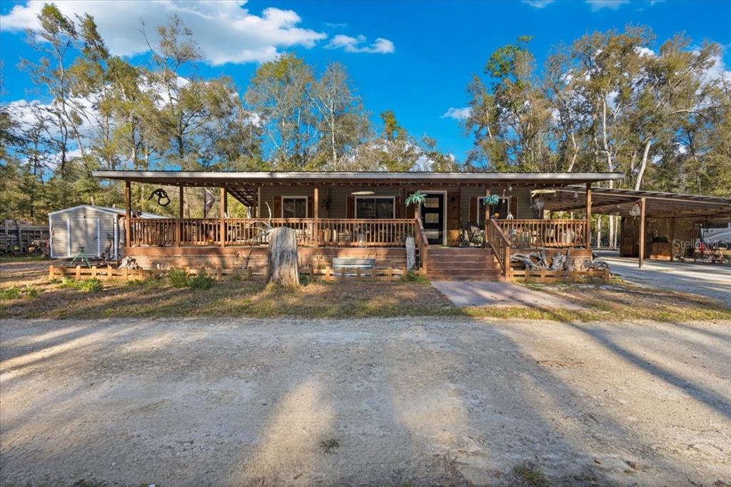 A single-story house with a large wooden porch sits on a dirt lot with trees — 5850 NW 50TH STREET, BELL, FL
