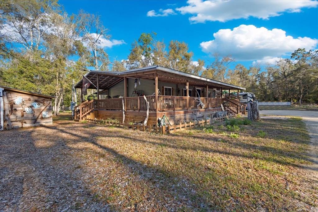 A single-story house with a large wraparound wooden porch sits on a wooded lot — 5850 NW 50TH STREET, BELL, FL