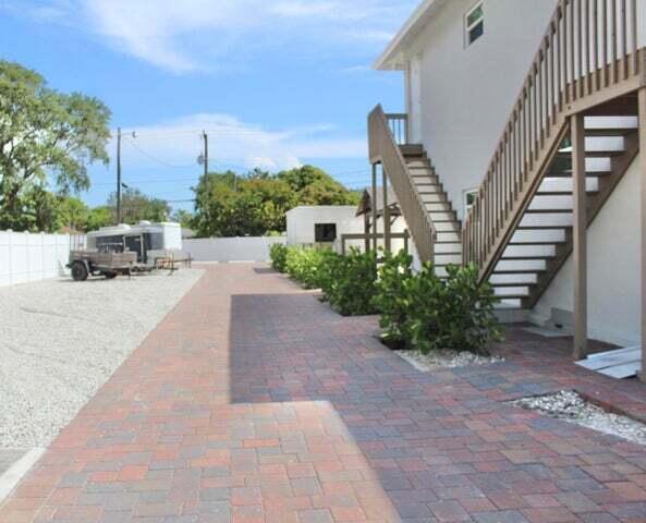 A paved walkway leads past a white building with an exterior staircase and gravel parking — 305 Cypress Drive # 1, Lake Park FL 33403, LAKE PARK, FL