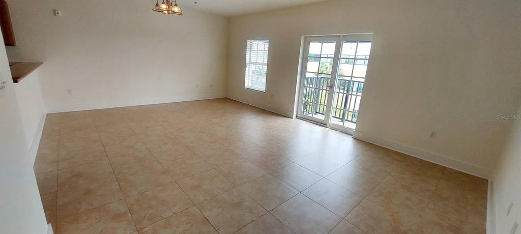 An empty living room features light-colored tile flooring, white walls, and a glass balcony door — 300 STATE STREET E UNIT 324, OLDSMAR, FL