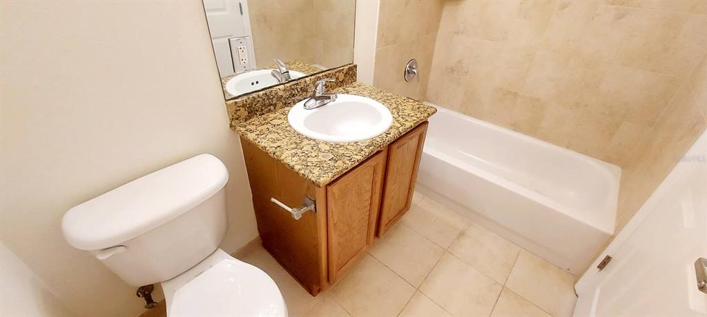 A bathroom features a granite vanity, a white toilet, and a tiled bathtub shower combination — 300 STATE STREET E UNIT 324, OLDSMAR, FL