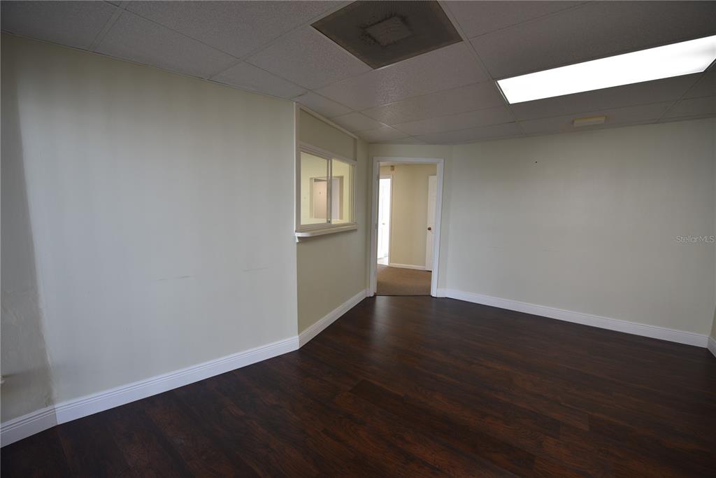 An empty room features dark wood-look flooring, light-colored walls, a drop ceiling, and a window — 1200 N CENTRAL AVENUE UNIT 212, KISSIMMEE, FL