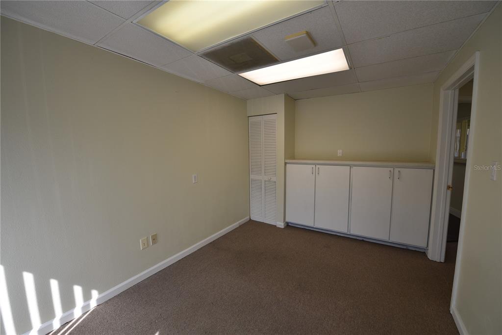 An office room features beige walls, brown carpeting, white built-in cabinets, and a drop ceiling — 1200 N CENTRAL AVENUE UNIT 212, KISSIMMEE, FL