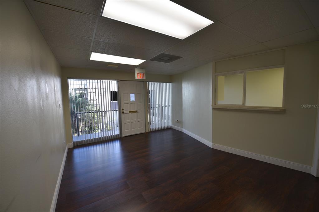 An empty office space features dark wood-look flooring, beige walls, and a white exit door — 1200 N CENTRAL AVENUE UNIT 212, KISSIMMEE, FL