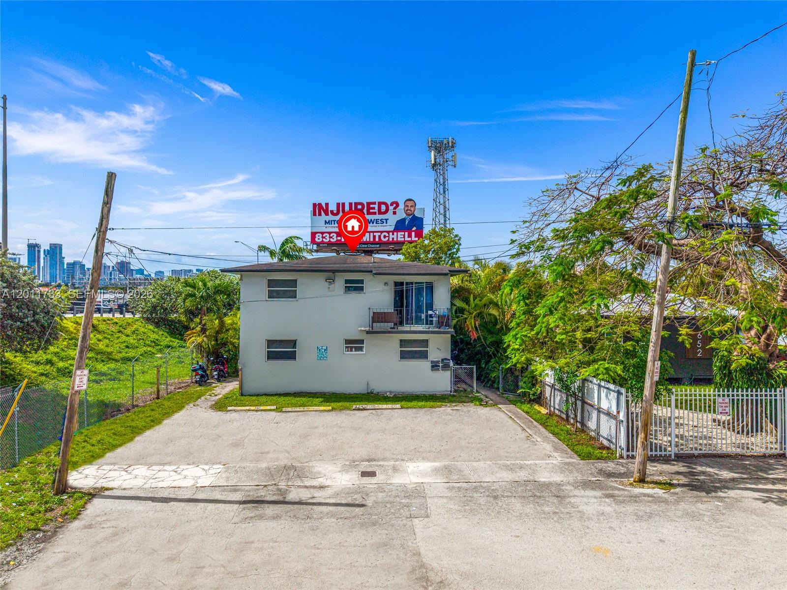 A two-story apartment building with a concrete parking lot sits beneath a large billboard — 650 NW 28th St, Miami FL 33127, MIAMI, FL