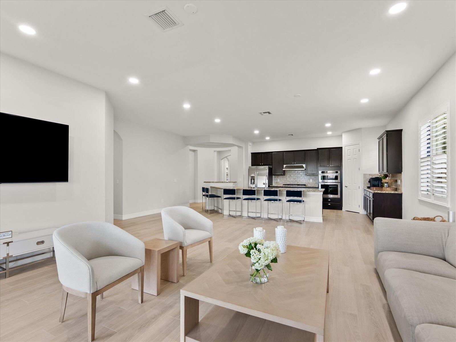 An open-concept living room features light wood flooring, a kitchen island with barstools, and cabinetry — 4452 Siena Circle, Wellington FL 33414, WELLINGTON, FL