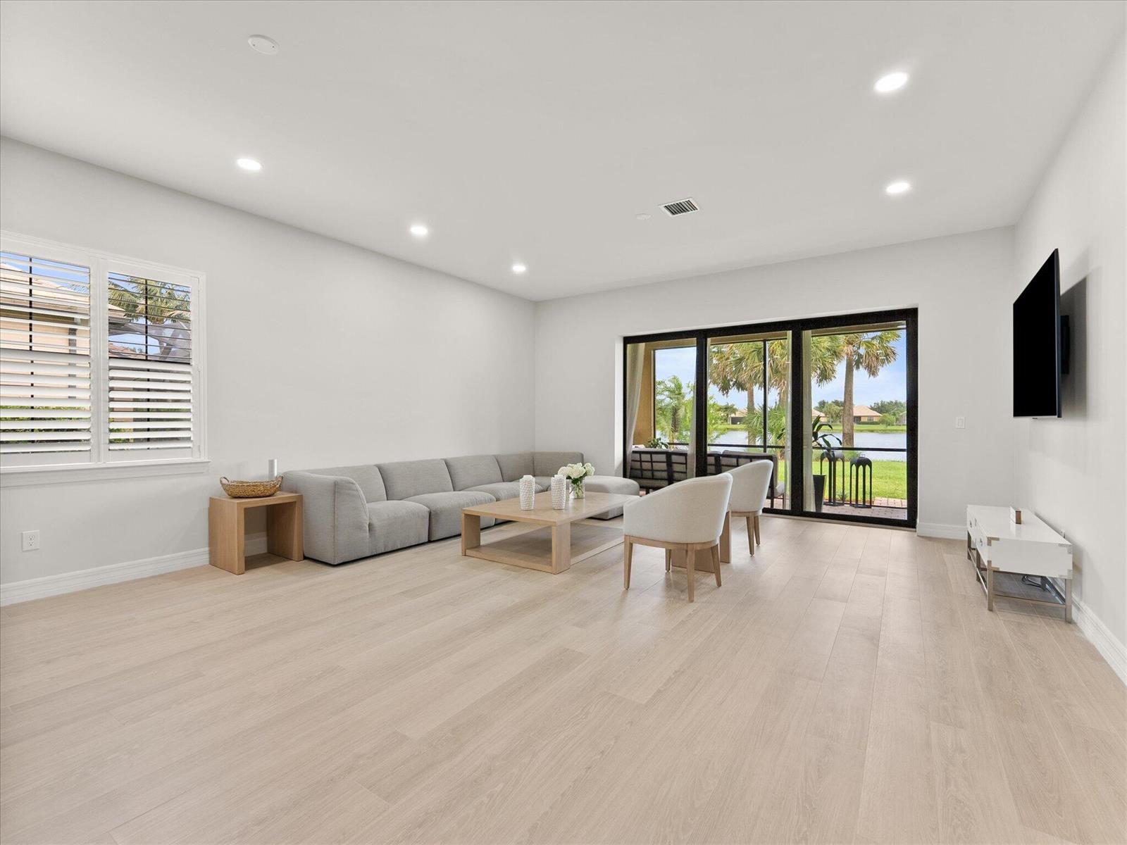 A bright living room features a gray sectional, light wood flooring, and sliding glass doors — 4452 Siena Circle, Wellington FL 33414, WELLINGTON, FL