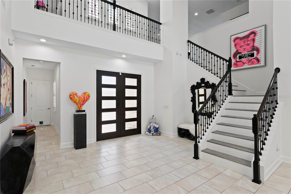 A bright, two-story foyer features white walls, tile flooring, a staircase, and modern art pieces — 7865 MARSH POINTE DRIVE, TAMPA, FL