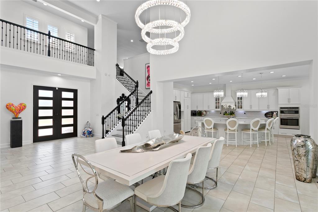 An open-concept dining room and kitchen feature white cabinetry, a tiered chandelier, and a staircase — 7865 MARSH POINTE DRIVE, TAMPA, FL
