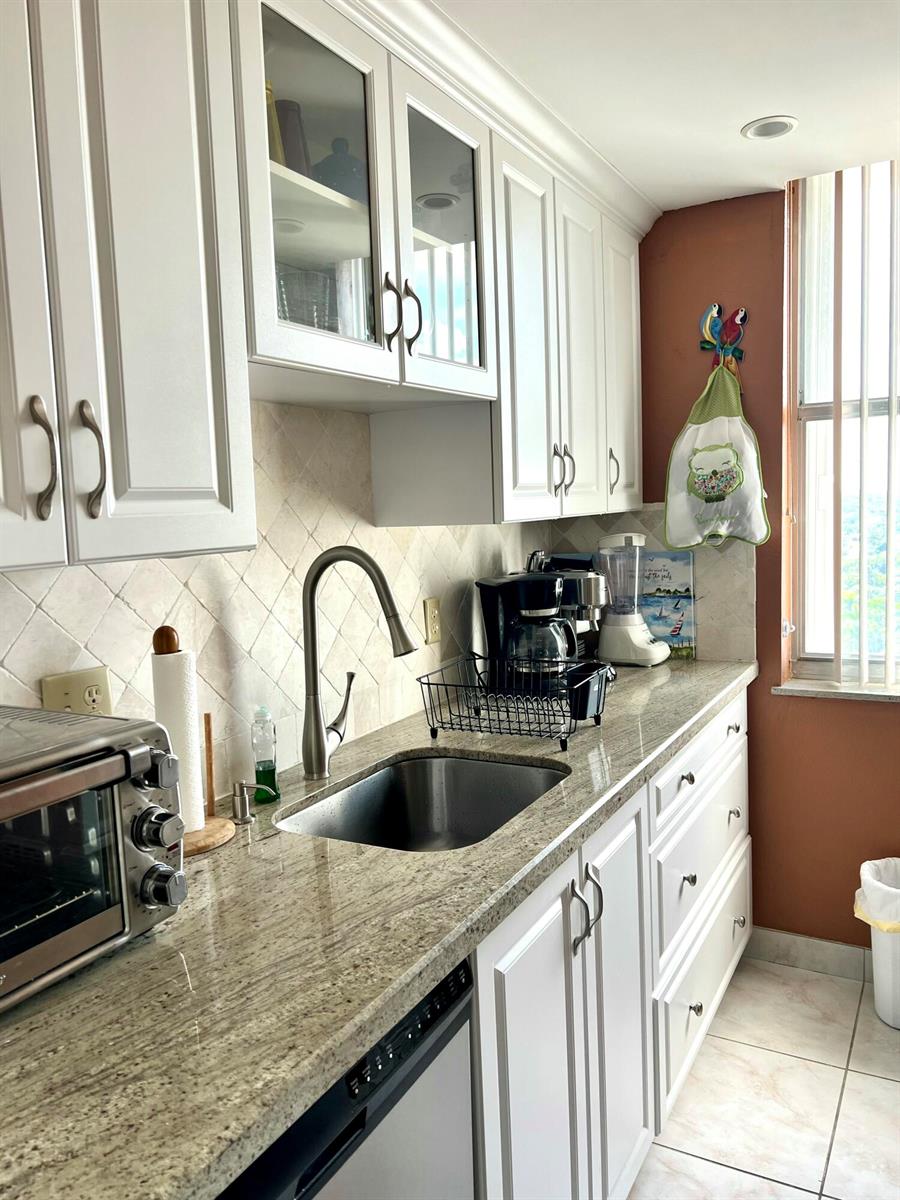 A kitchen features white cabinets, granite countertops, a stainless steel sink, and a tiled backsplash — 111 Briny Avenue # 1511, Pompano Beach FL 33062, POMPANO BEACH, FL