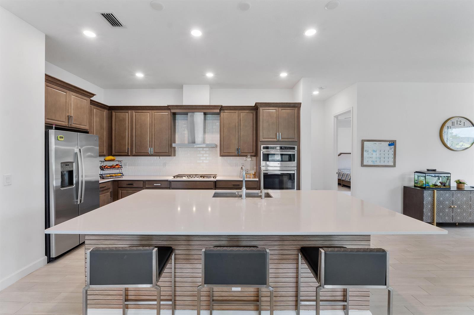 A modern kitchen features a large quartz island, dark wood cabinets, and stainless steel appliances — 19036 Broad Shore Walk, FL 33470, FL