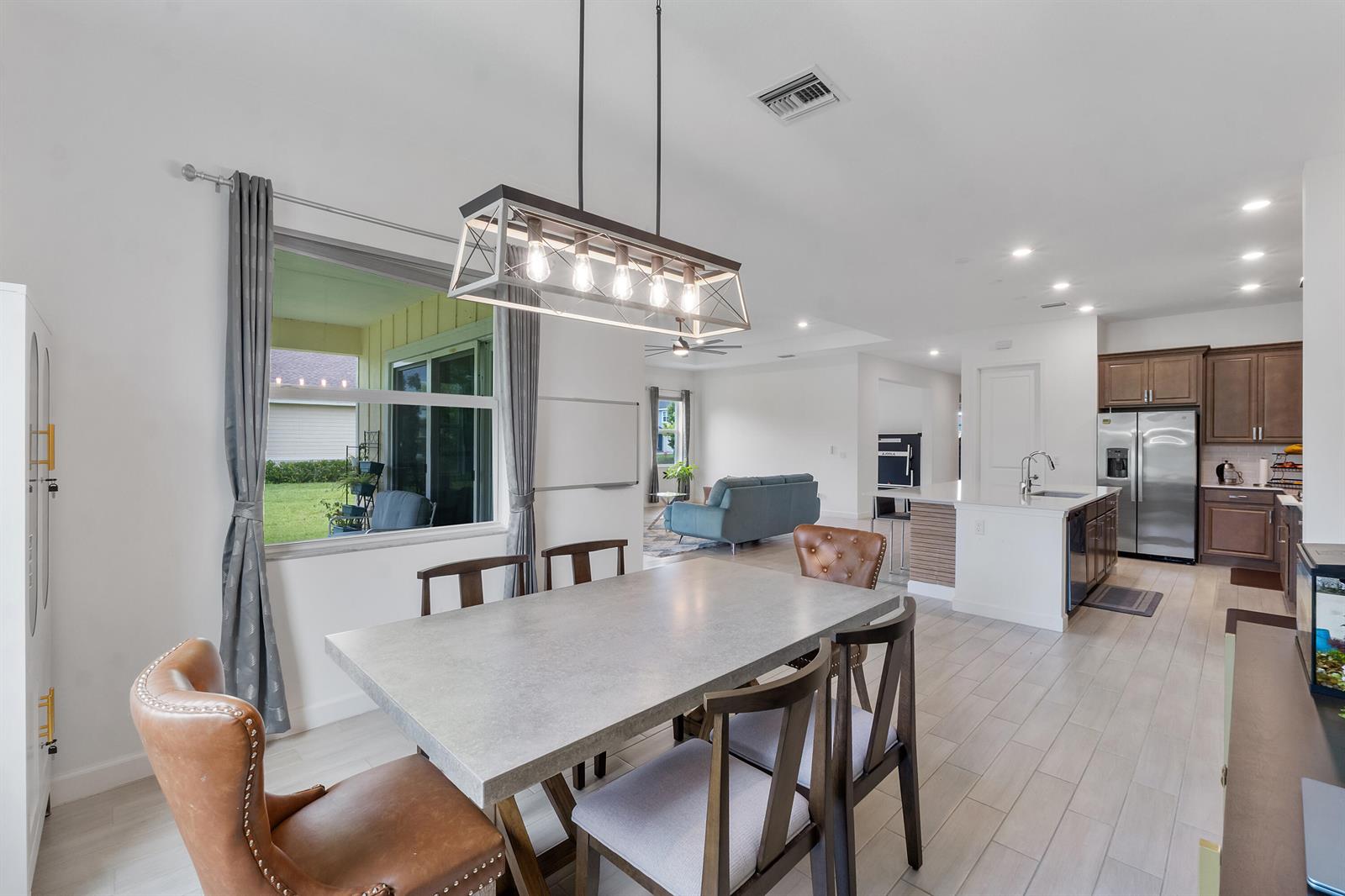 A dining area with a concrete table and pendant light opens to a modern kitchen — 19036 Broad Shore Walk, FL 33470, FL