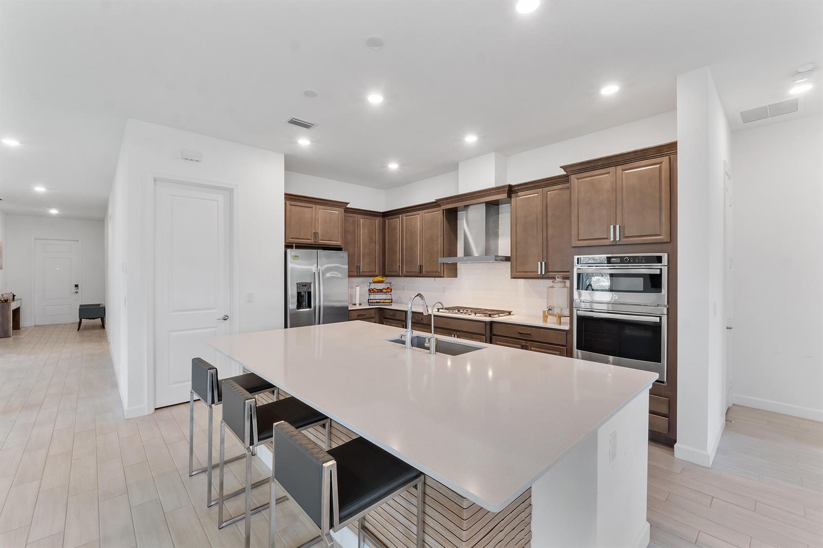 A modern kitchen features a large quartz island, dark wood cabinetry, and stainless steel appliances — 19036 Broad Shore Walk, FL 33470, FL