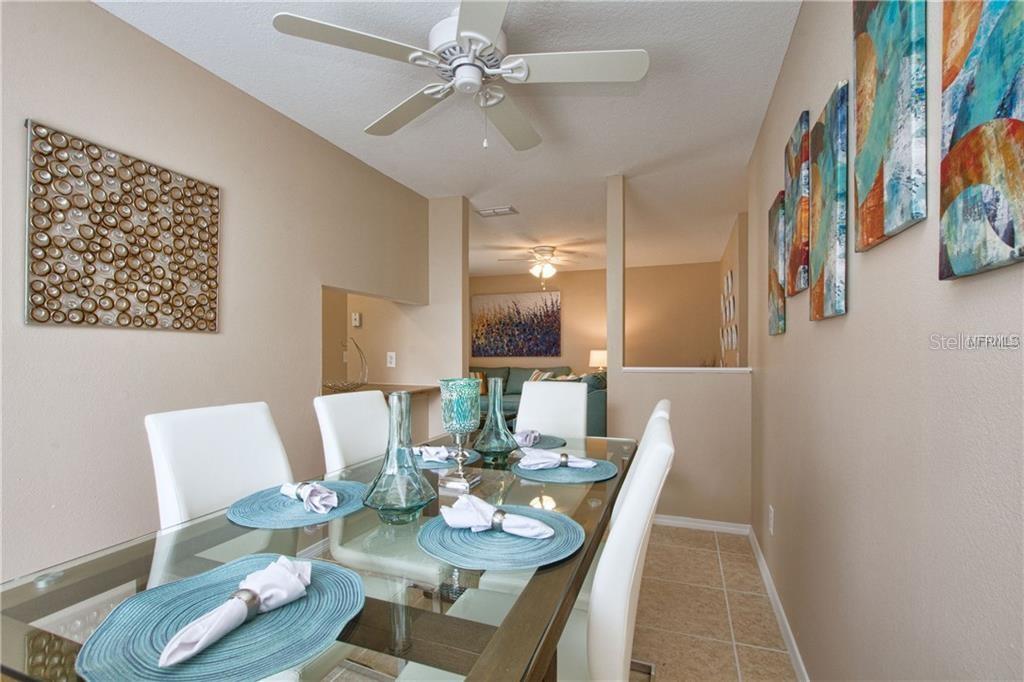 A dining room features a glass table, white chairs, and wall art on beige walls — 4160 PERSHING POINTE PLACE UNIT 1, ORLANDO, FL