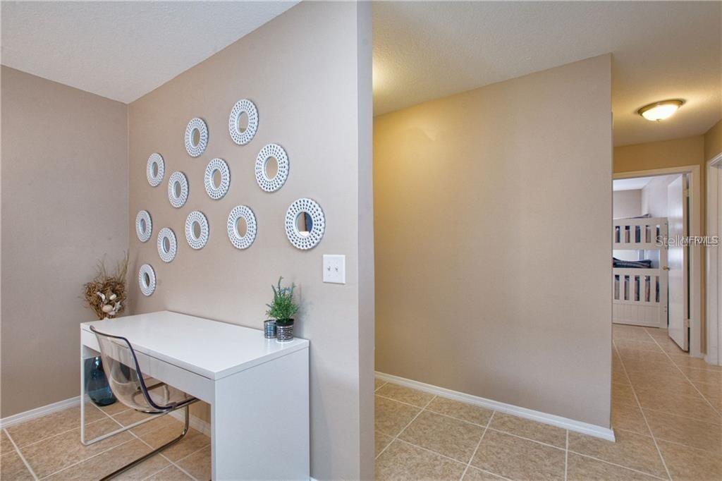 A white desk sits against a wall decorated with circular wall art in a hallway — 4160 PERSHING POINTE PLACE UNIT 1, ORLANDO, FL