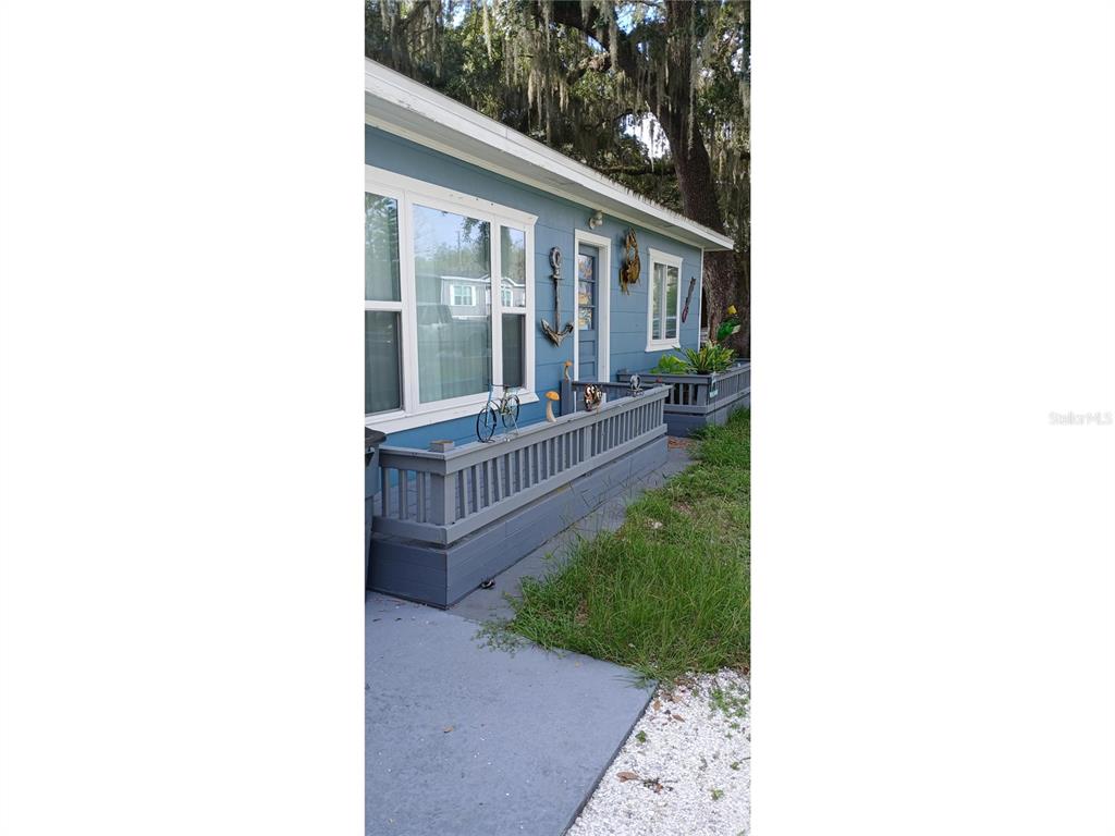 A blue house exterior features a wooden porch railing, decorative wall hangings, and large windows — 7804 CHASCO STREET, PORT RICHEY, FL