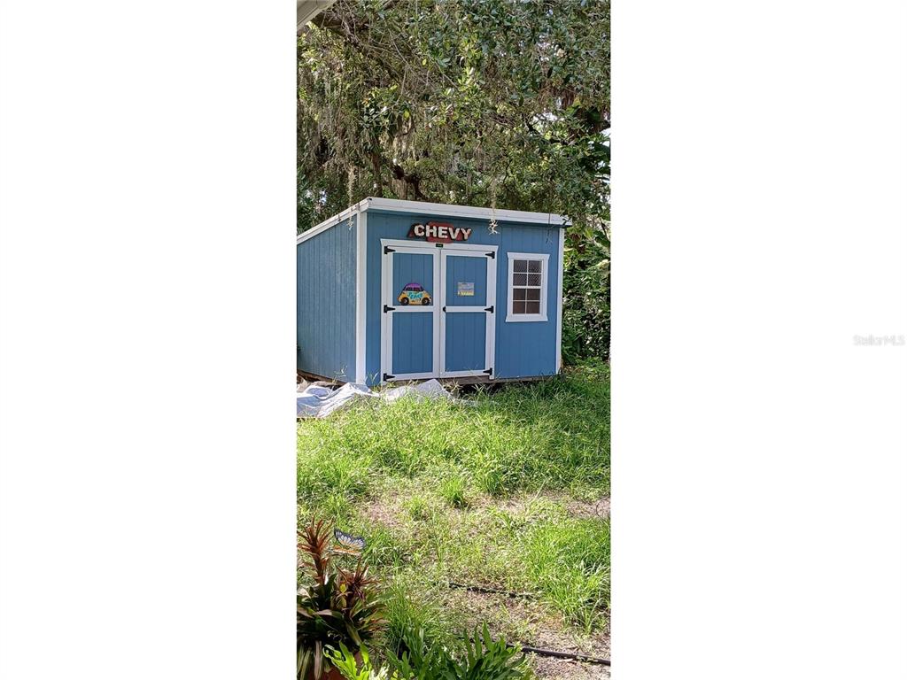 A blue wooden storage shed with double doors and a window sits in a grassy yard — 7804 CHASCO STREET, PORT RICHEY, FL