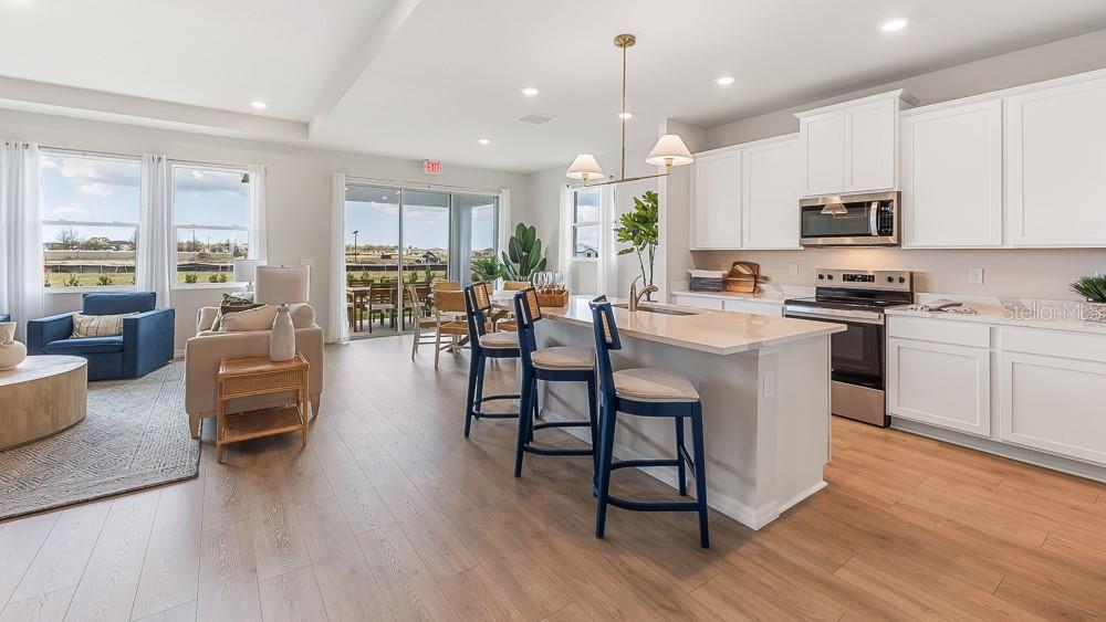 A bright open-concept kitchen and living area features white cabinetry, a kitchen island, and flooring — 11909 KINGSLEY TRAIL, PARRISH, FL