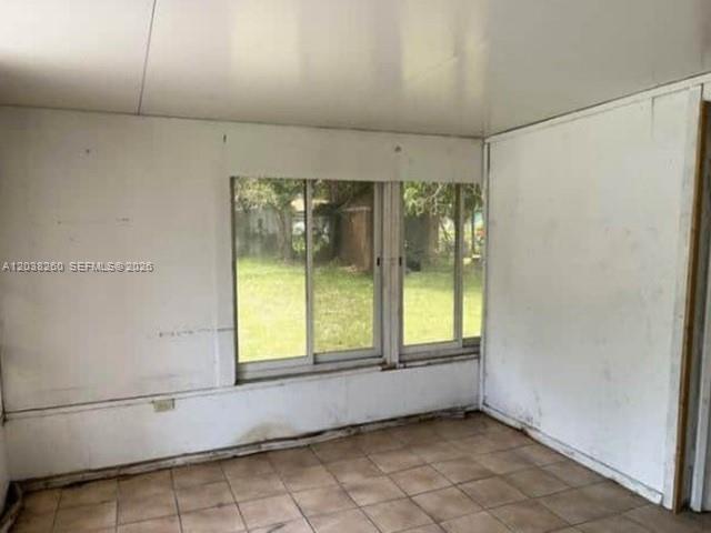 An empty room with white paneled walls, tiled floors, and windows overlooking a grassy yard — 314 S 17th St, Fort Pierce FL 34950, FORT PIERCE, FL