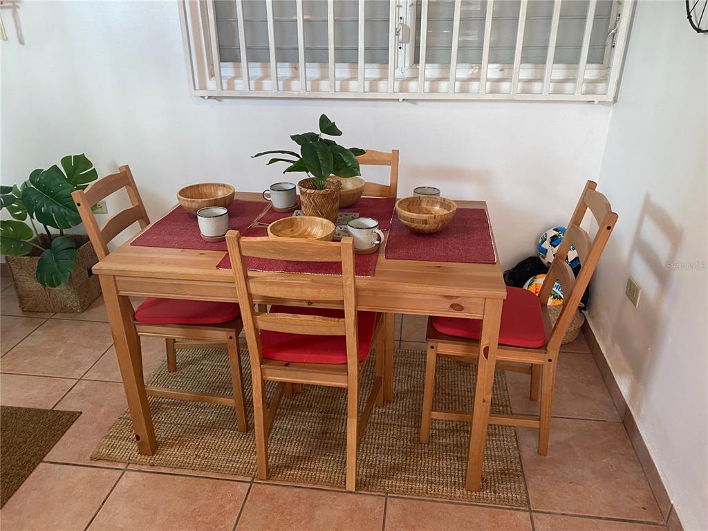 A wooden dining table with four chairs sits on a rug in a tiled room — 14 JOSE JULIAN ACOSTA Apt E1, VEGA BAJA, PR