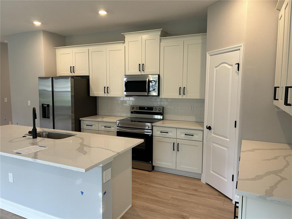 A modern kitchen features white cabinets, stainless steel appliances, and a quartz-topped island — 41 GREENTREE STREET, HOMOSASSA, FL