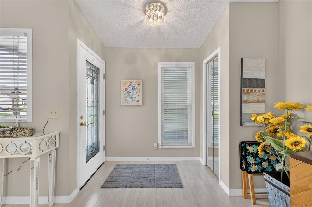 A bright entryway features light wood-look flooring, a white front door, and a central rug — 731 CORTEZ AVENUE, LADY LAKE, FL