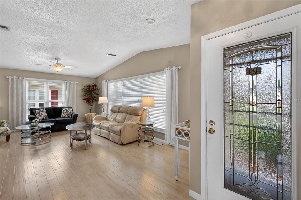 A living room with light wood floors, a beige sofa, and a glass-paneled front door — 731 CORTEZ AVENUE, LADY LAKE, FL