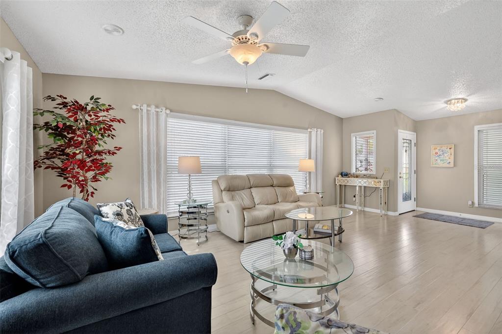 A living room features light wood flooring, a blue sofa, a beige loveseat, and a ceiling fan — 731 CORTEZ AVENUE, LADY LAKE, FL