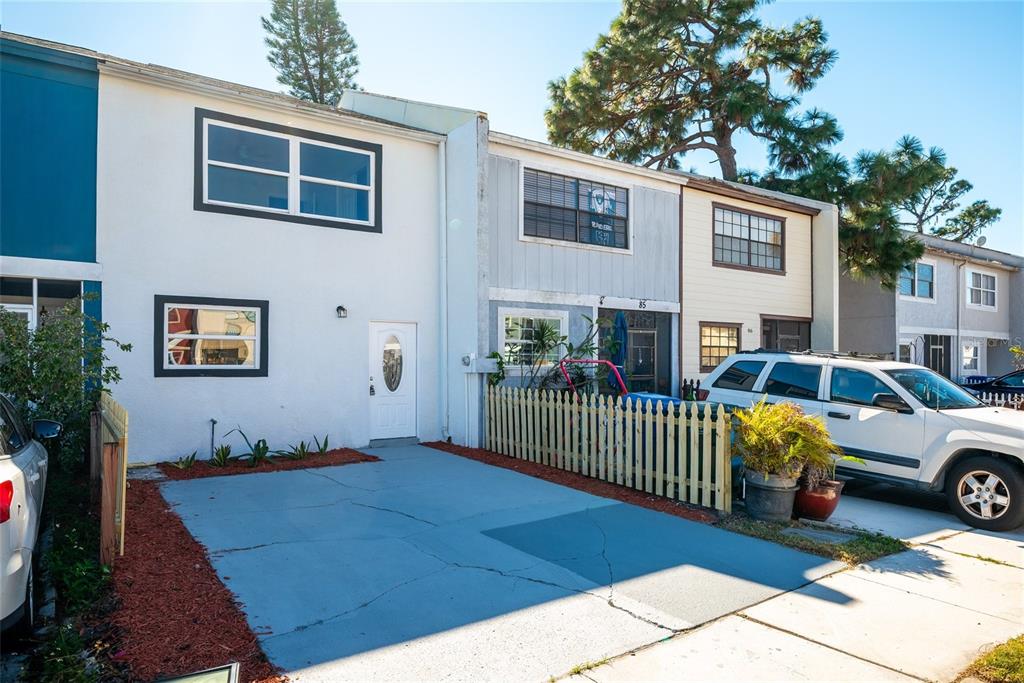 The exterior of a multi-story townhouse features a blue-painted driveway and a white picket fence — 3150 S PINES DRIVE UNIT 84, LARGO, FL